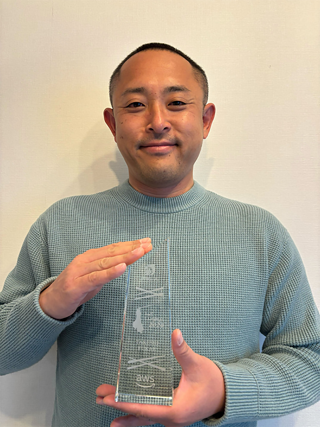 A person holding an AWS Samurai 2024 award trophy and smiling at the camera.