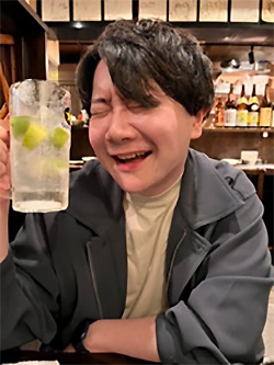 A person smiling and holding a glass with lime slices at a restaurant, with a warm and lively indoor atmosphere.