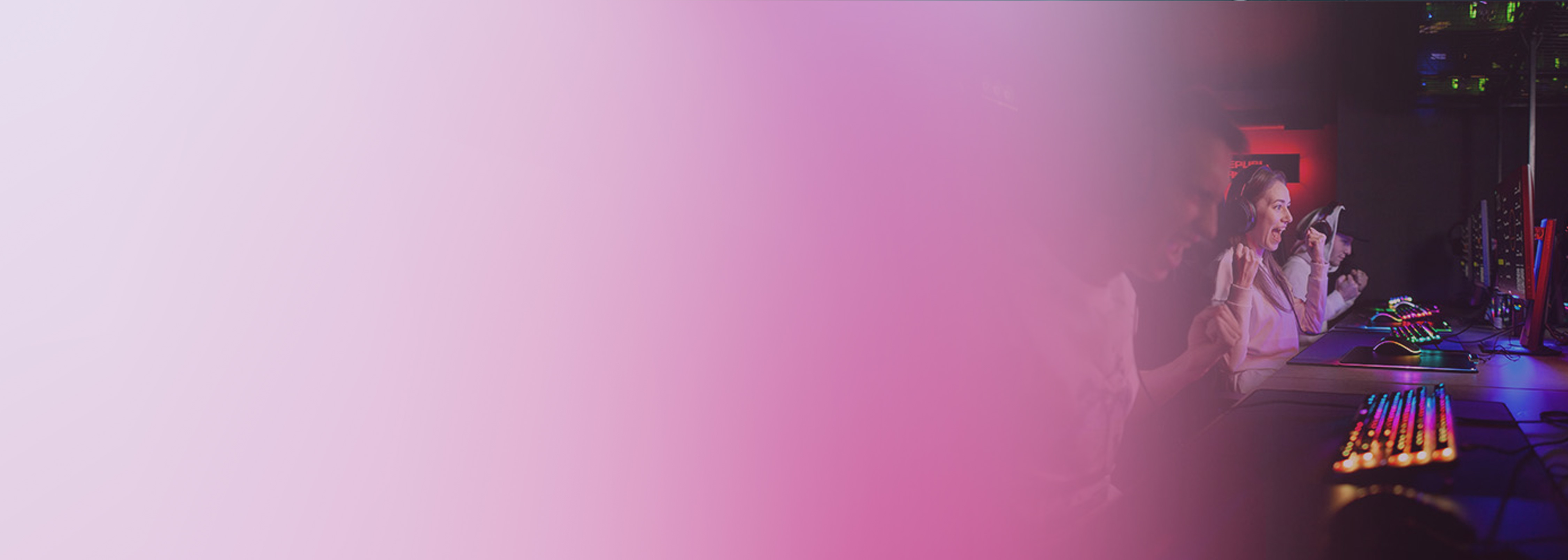 A group of excited gamers wearing headsets playing multiplayer games on desktop computers in a gaming room, with a pink gradient overlay on the left side of the image.