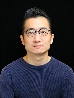 A portrait of an individual wearing glasses and a dark sweater, set against a dark background.