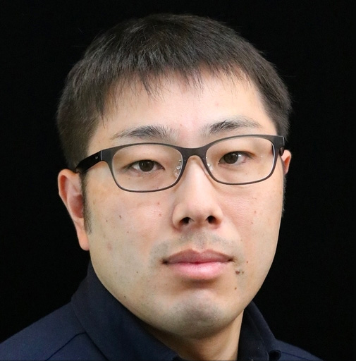 A portrait photo of a man with short hair and glasses, posed in front of a black background.