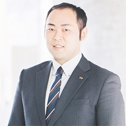 A professional business portrait of a man in a suit and tie, standing in a bright, modern office environment.
