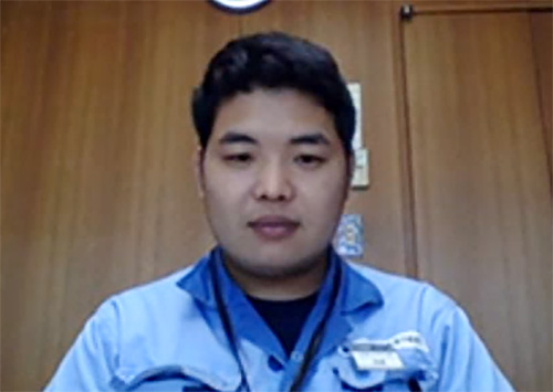 A man wearing a blue uniform sitting indoors in front of a wooden wall.