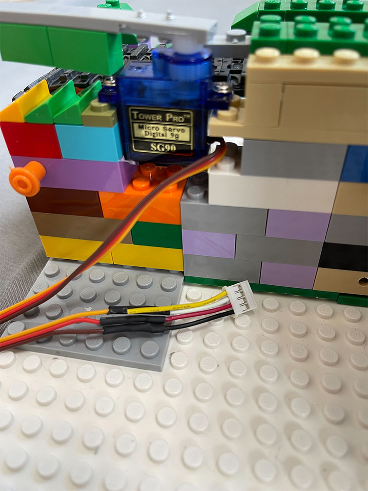 Closeup photo of a Tower Pro SG90 micro servo motor connected with wiring, built into a colorful LEGO brick assembly.