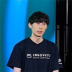 Portrait of a speaker at the AWS Innovate Online Conference wearing an AWS Innovate t-shirt, standing against a blue and black background.