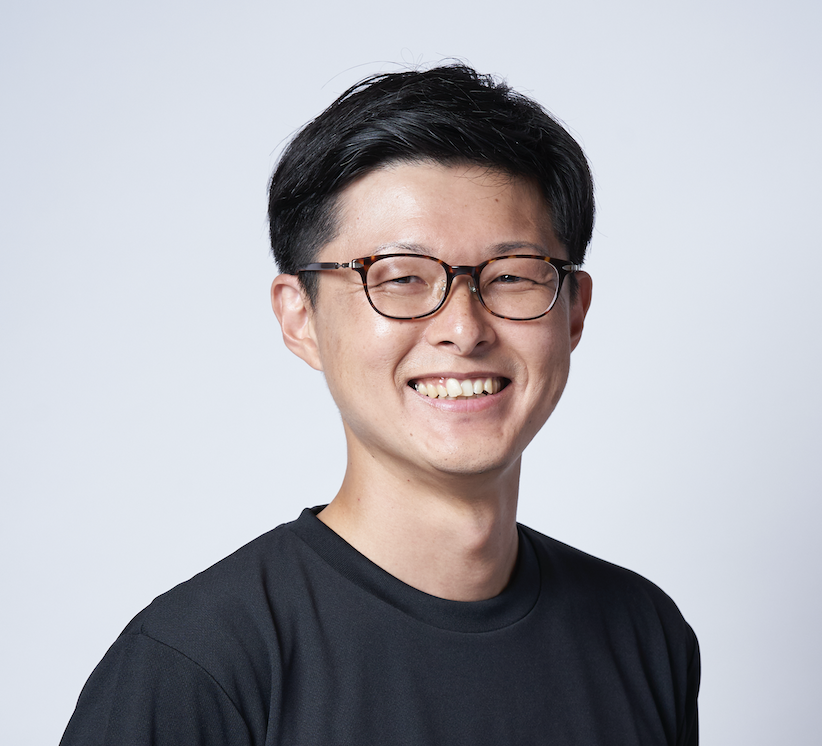 Portrait of a man wearing glasses and a black shirt, smiling at the camera, on a light background.