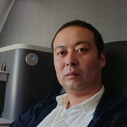A portrait photo of a man sitting in a professional business environment, wearing a white shirt and dark jacket.