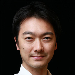 A professional headshot of an individual with short dark hair, wearing a white shirt and facing the camera, set against a black background.