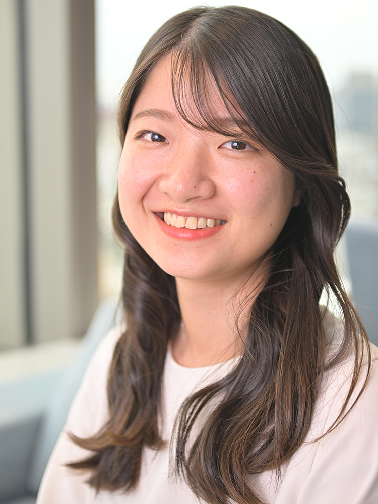 A young woman with long hair smiling, photographed indoors in natural light. The background is softly blurred, providing a warm, professional atmosphere.
