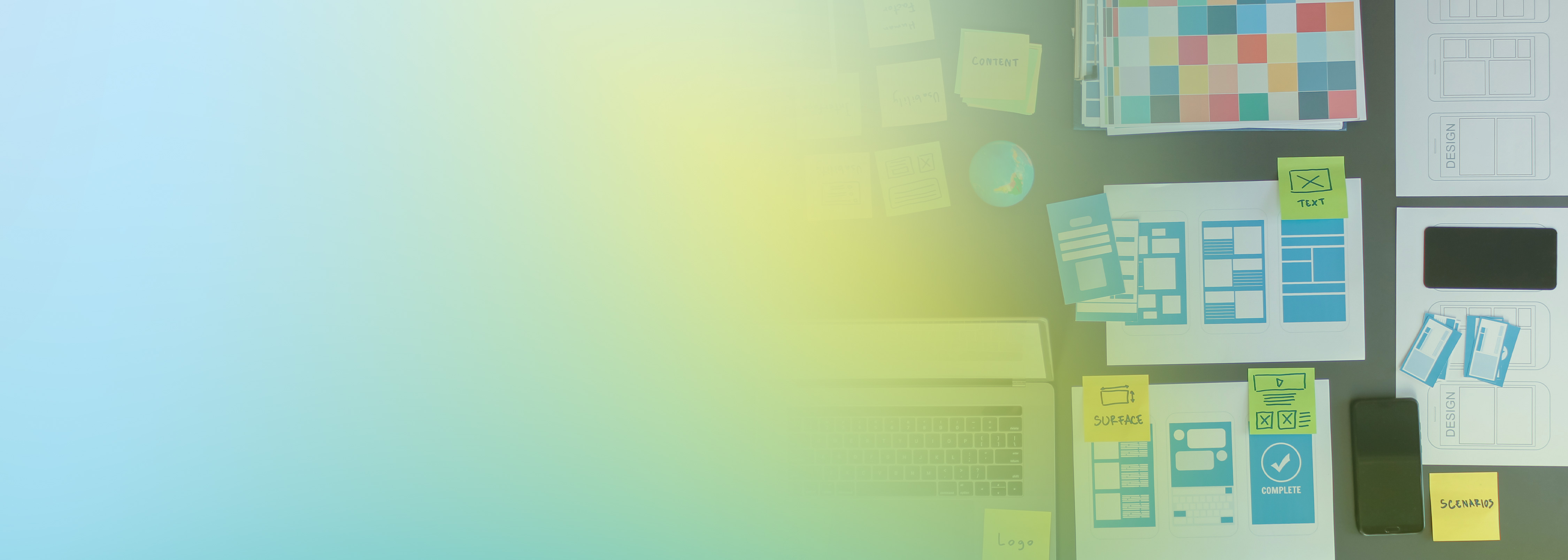 Top view of a workspace showing papers with wireframes, design plans, a laptop, mobile device, and sticky notes, representing distributed test planning and application design on AWS.