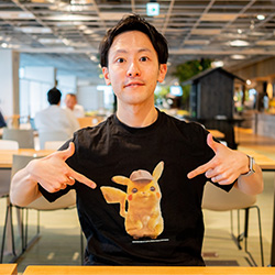 A man sitting at a table in a cafe, pointing at a t-shirt featuring Detective Pikachu.