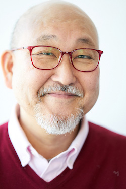 A portrait photograph of a smiling man wearing glasses, a beard, and a red sweater over a pink shirt. The image is titled 'Portrait of Fukui Atsushi, 2021.'