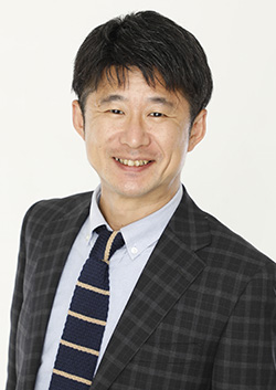 A professional business portrait of a man in a dark plaid suit and striped tie, smiling and facing the camera against a light background.