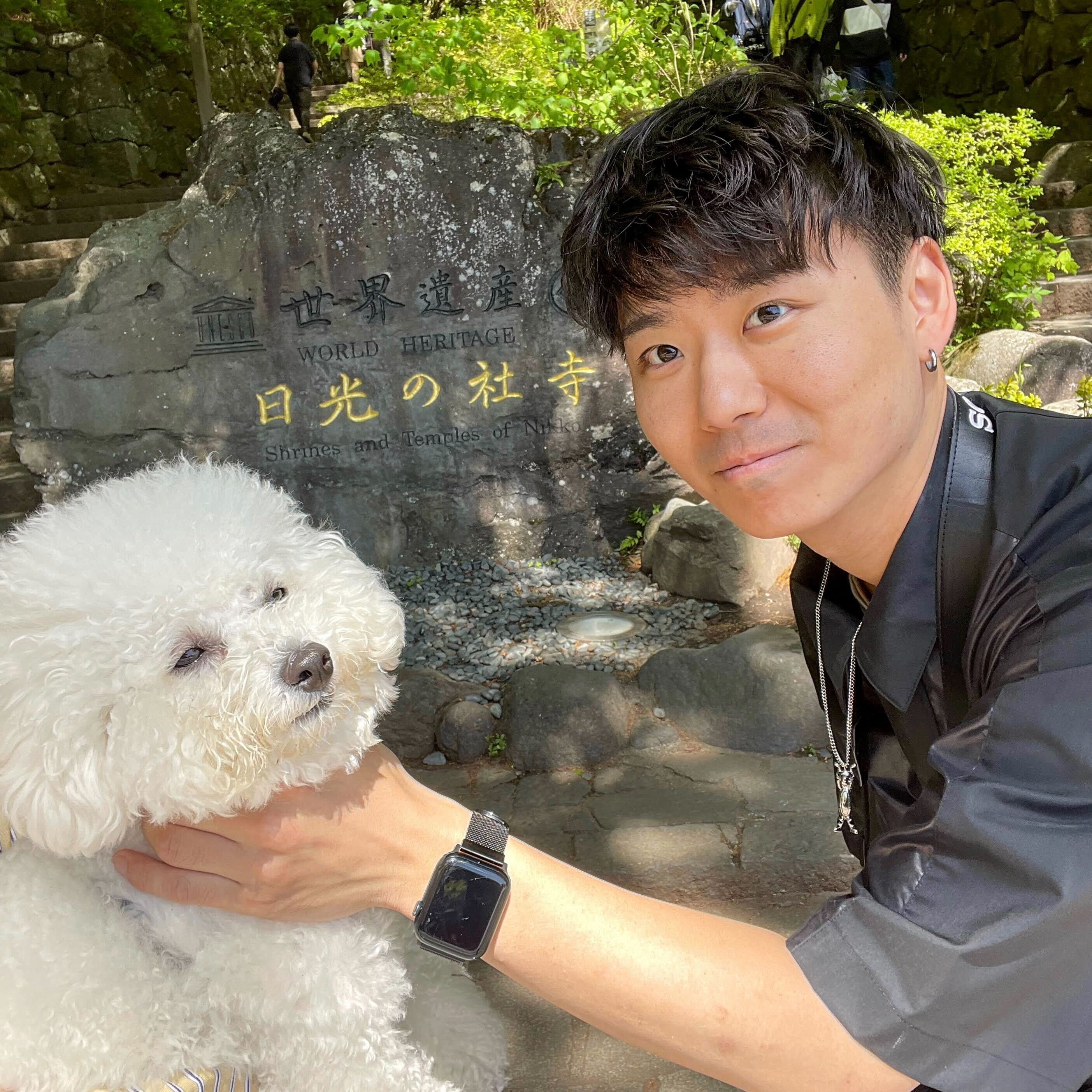 A man poses with a fluffy white dog in front of a stone sign for the Nikko World Heritage shrines and temples in Japan.