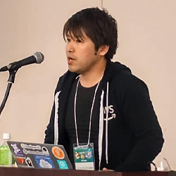 A person standing at a podium with a laptop, speaking into a microphone at a conference.