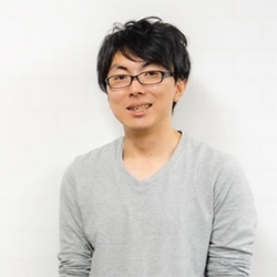 Portrait of a man in a gray shirt with glasses, standing in a casual pose against a white background