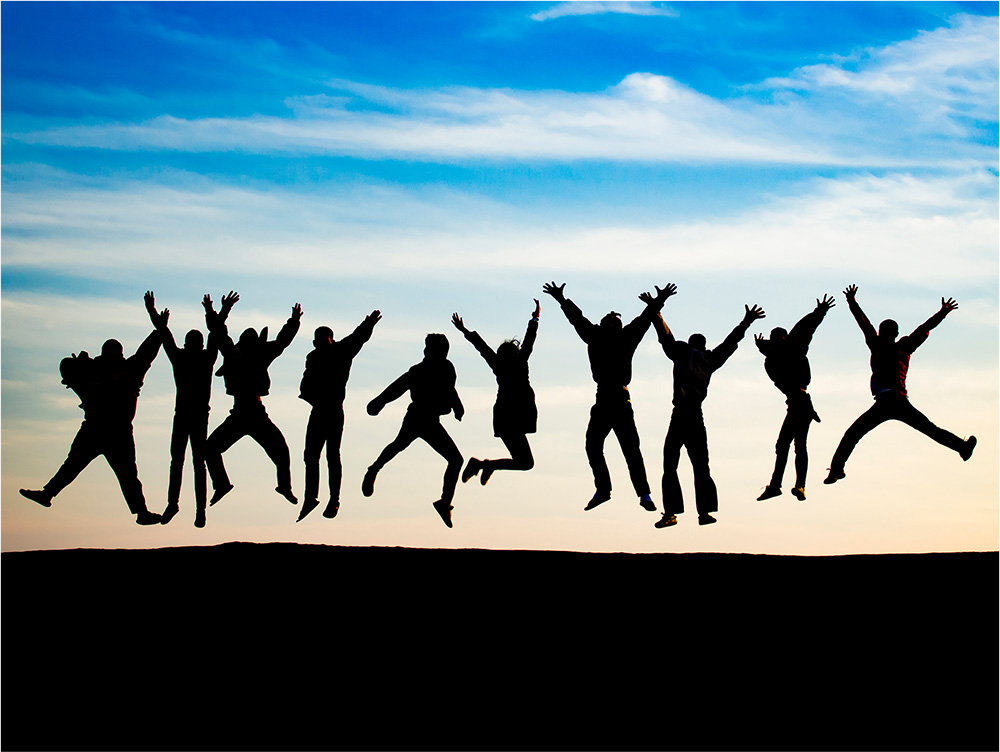 A group of people silhouetted against a colorful sunset sky, all jumping in the air with arms raised, conveying a sense of joy and togetherness.