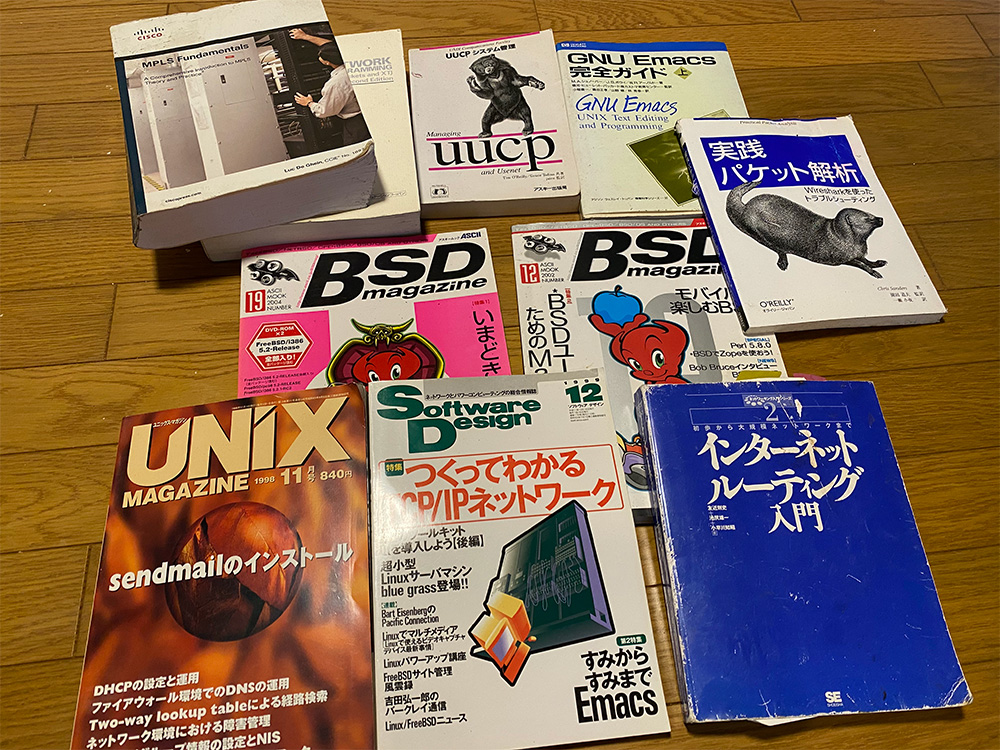 A collection of vintage Japanese networking and UNIX books and magazines, including titles on Unix, BSD, Emacs, packet analysis, and network fundamentals, arranged on a wooden floor.