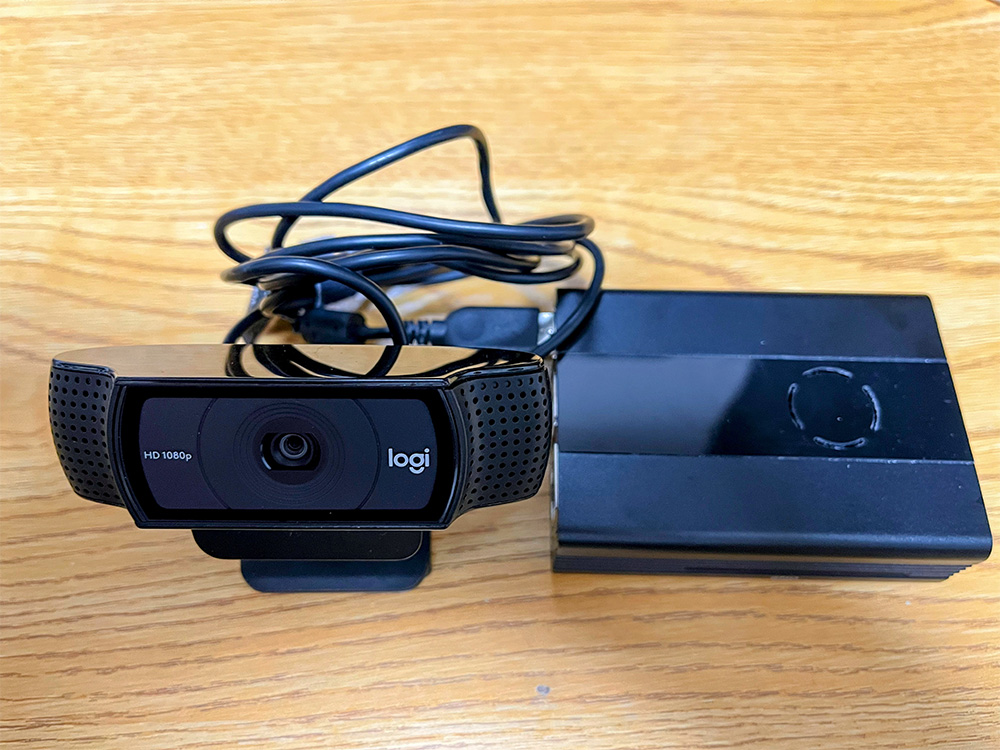 A Logitech HD 1080p webcam and an external hard drive placed side by side on a wooden desk.