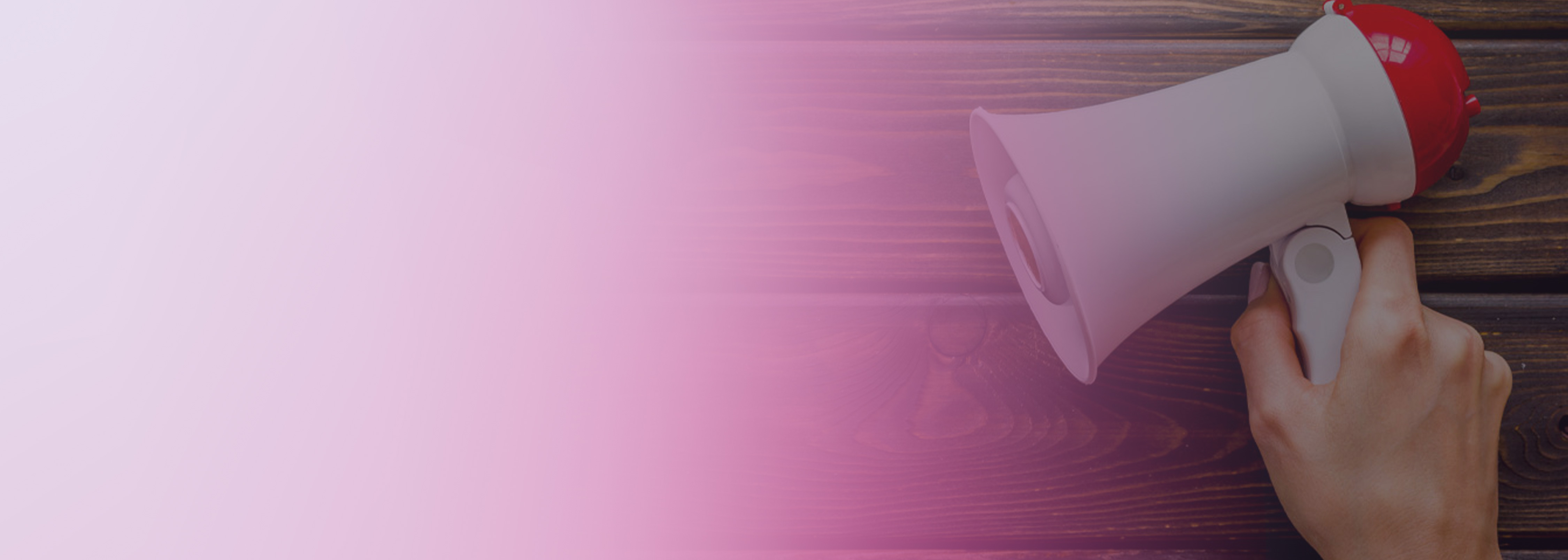 A hand holding a white and red megaphone on a wooden surface with a pink gradient overlay on the left side of the image.