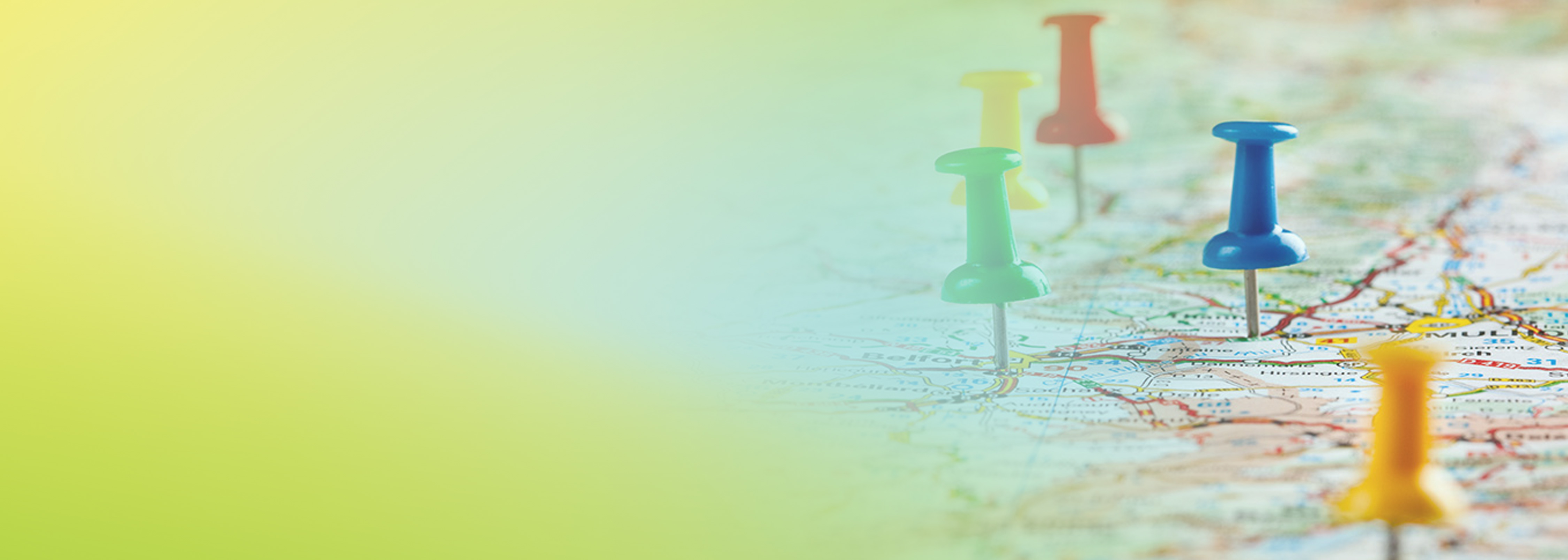A close-up image of a map with various colored push pins (green, blue, yellow, and red) marking different locations. The background features a yellow-green gradient overlay on the left side of the image.