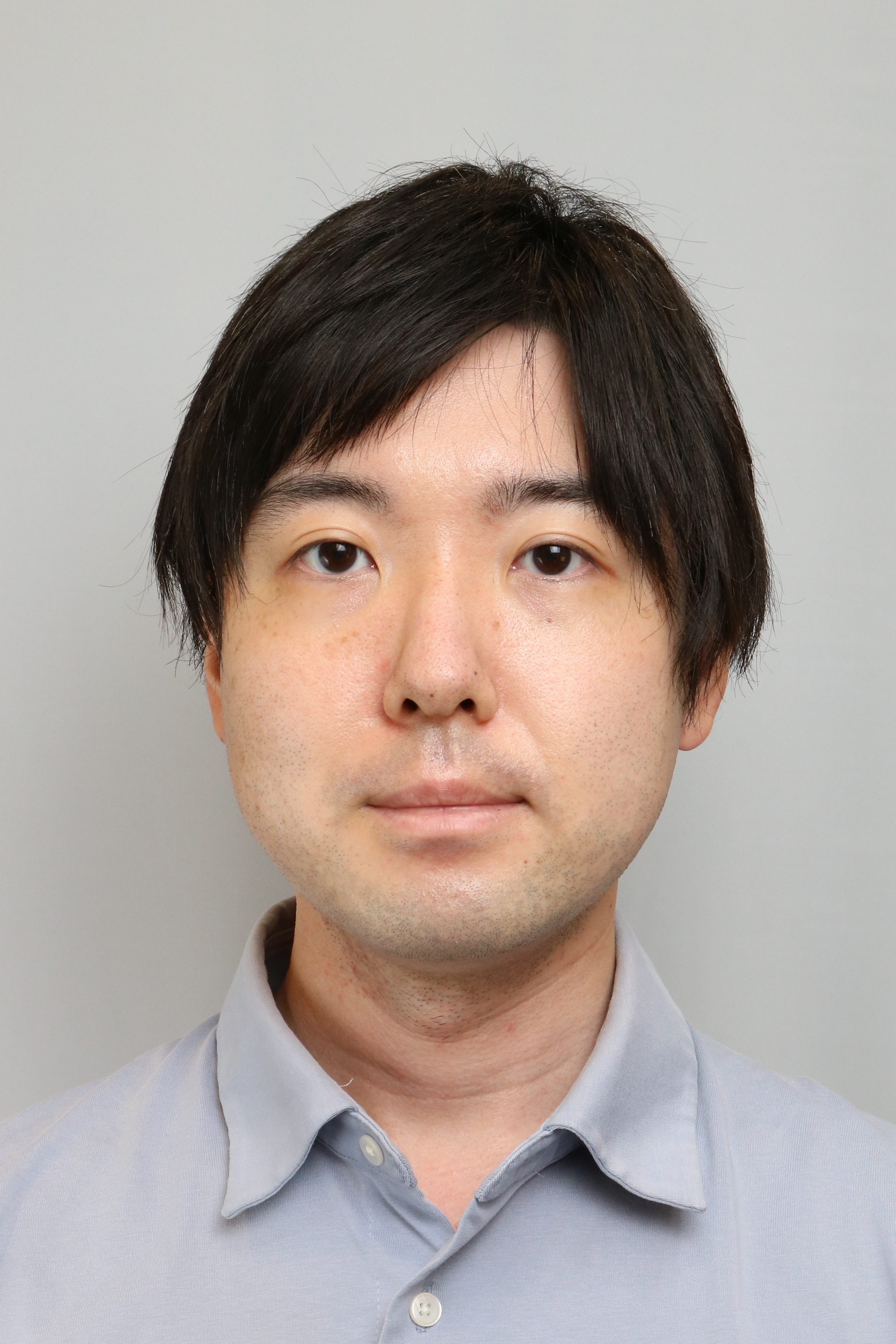 A portrait photo of an individual with short dark hair wearing a light grey shirt, against a plain background.