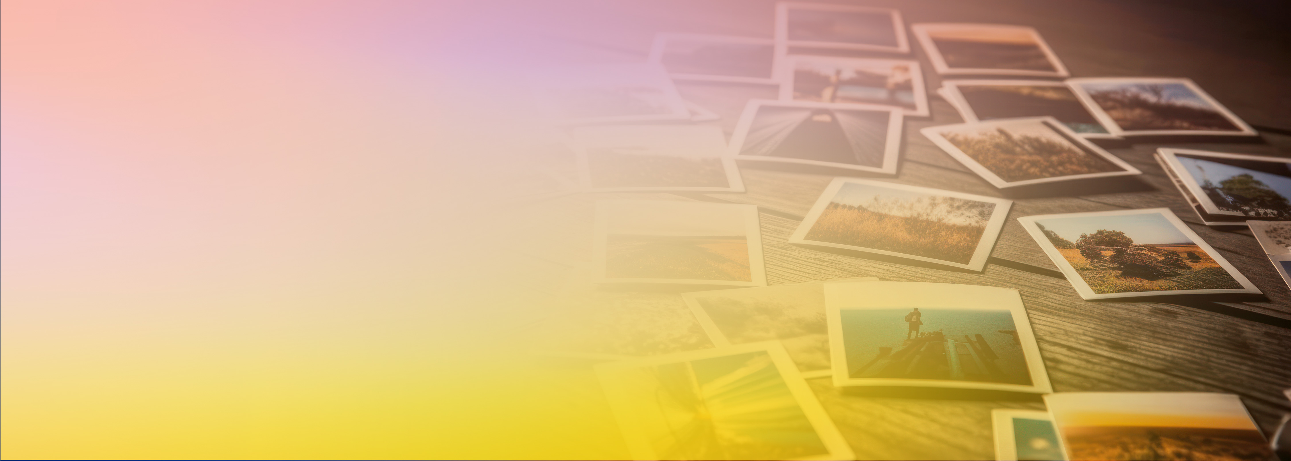 A collection of printed photographs scattered on a wooden surface, partially overlaid by a soft gradient of yellow and pink pastel colors.
