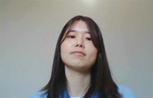Portrait of a woman with long dark hair wearing a blue top, facing forward with a neutral expression against a plain background.