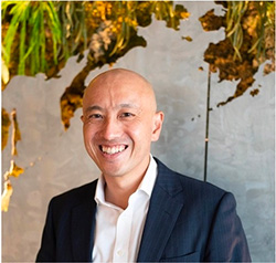 A smiling business professional in a suit poses for a portrait in front of an artistic wall background.