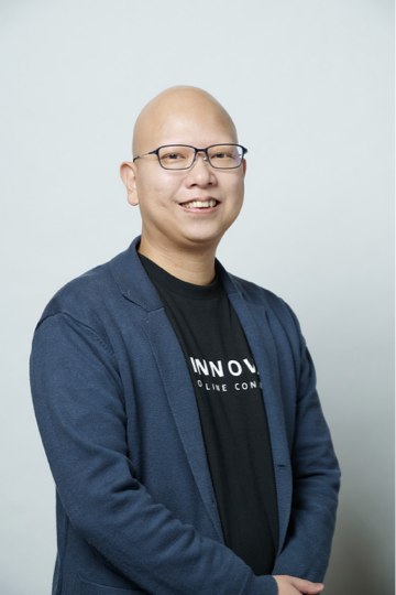 A smiling bald man wearing glasses and a blue blazer, posing against a plain light background.
