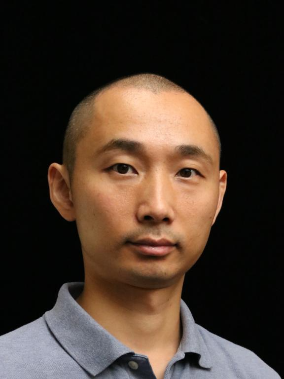 A portrait of a man in a gray polo shirt against a black background