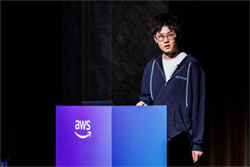 A speaker presenting at an AWS event, standing behind a podium displaying the AWS logo.