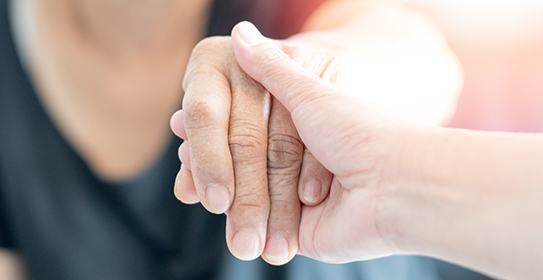 A close-up image of one person gently holding another person's hand, symbolizing care, support, and compassion.