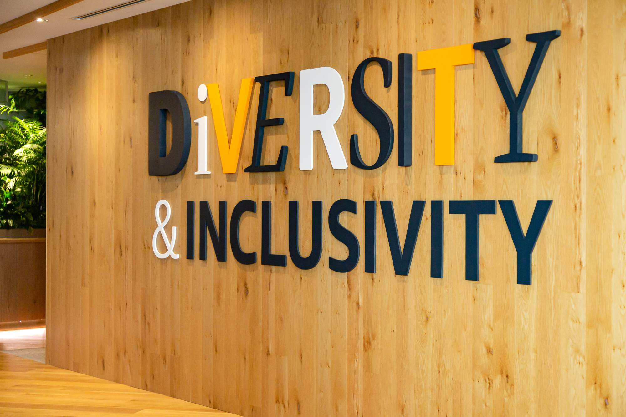Text on a wooden wall reads "Diversity & Inclusivity" in bold letters, with greenery visible in the background.