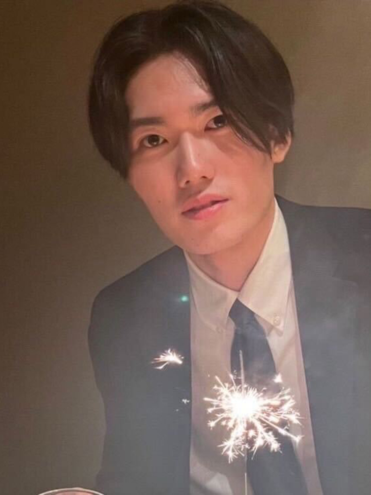 A man wearing a suit is holding a lit sparkler, looking at the camera.
