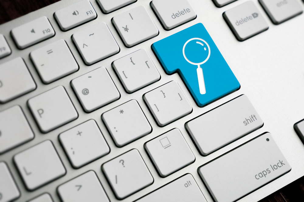 A close-up image of a computer keyboard with a blue key featuring a magnifying glass search icon, symbolizing search functionality or online search.