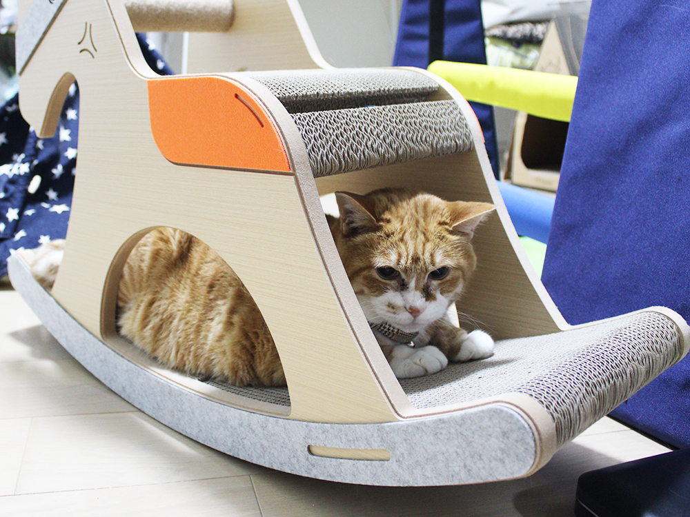 An orange tabby cat lying inside a wooden rocking horse-shaped cat scratcher.