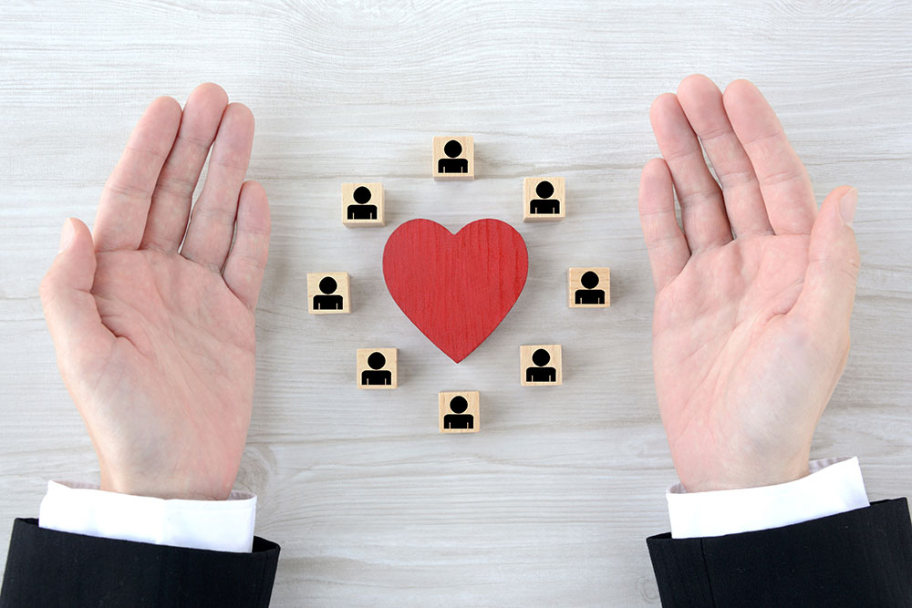 Concept image showing two hands encircling a red heart and small wooden blocks with people icons, symbolizing employee retention, protection, and care in the workplace.