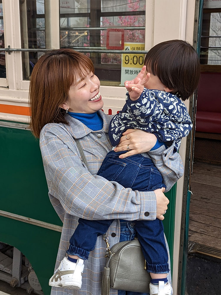 A mother holding her child and smiling while standing outside a tram. The scene captures a joyful moment between the parent and child.