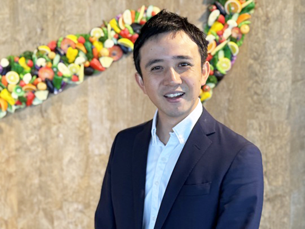 A man in a suit standing in front of a decorative background made of various fruits.