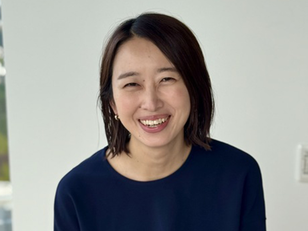A smiling woman with dark hair wearing a navy top, photographed indoors against a light background.