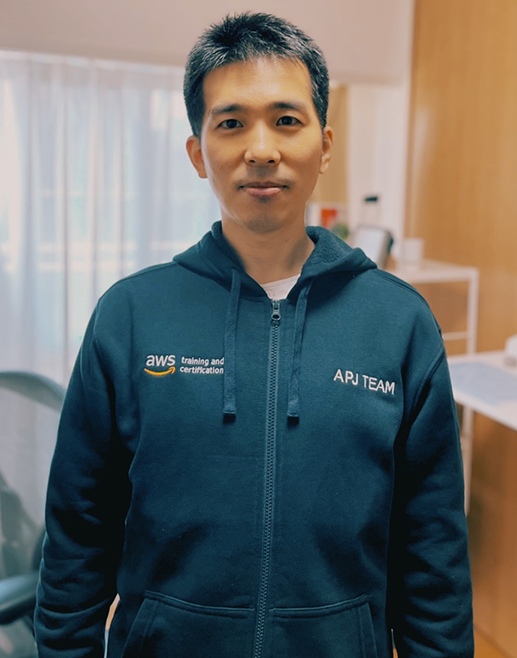 A member of the AWS Training and Certification APJ team standing indoors, wearing an AWS team hoodie.