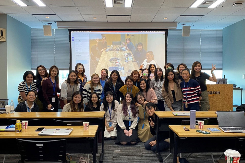 Group photo of women employees at Amazon's Japan office, taken in 2024, showing a diverse group of women gathered together in a meeting room with a projector screen in the background.