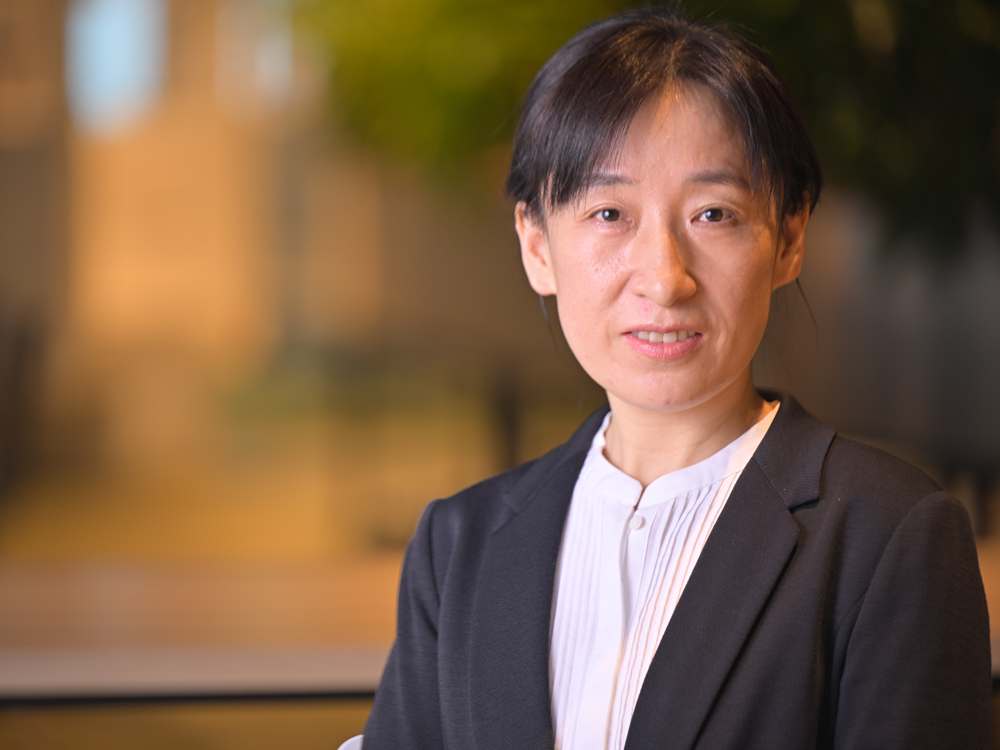 A professional portrait of a woman wearing business attire, photographed in an office setting with a blurred background.