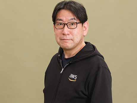 A portrait of an AWS employee wearing glasses and a black AWS hoodie, standing in front of a plain background.