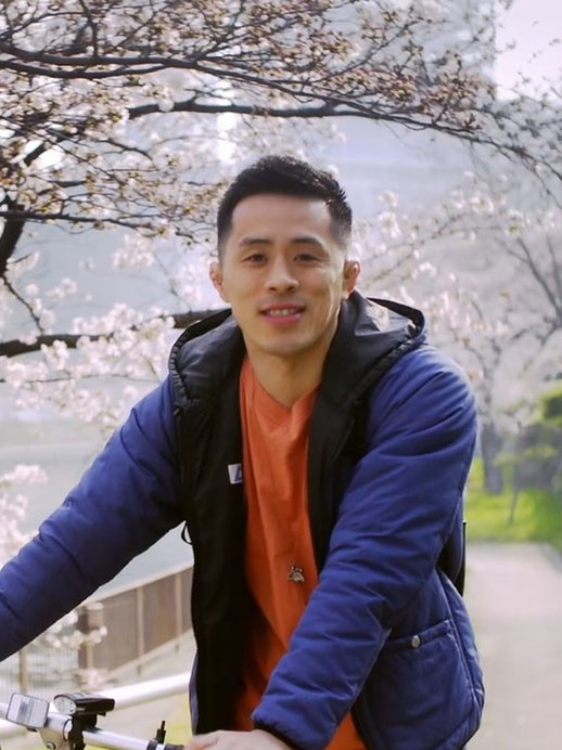A man riding a bicycle outdoors under blooming cherry blossom trees during spring.