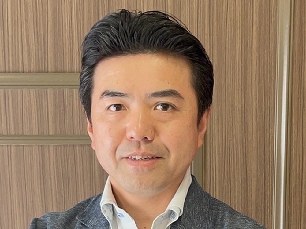 A man in business attire posing in front of a wood panel background.
