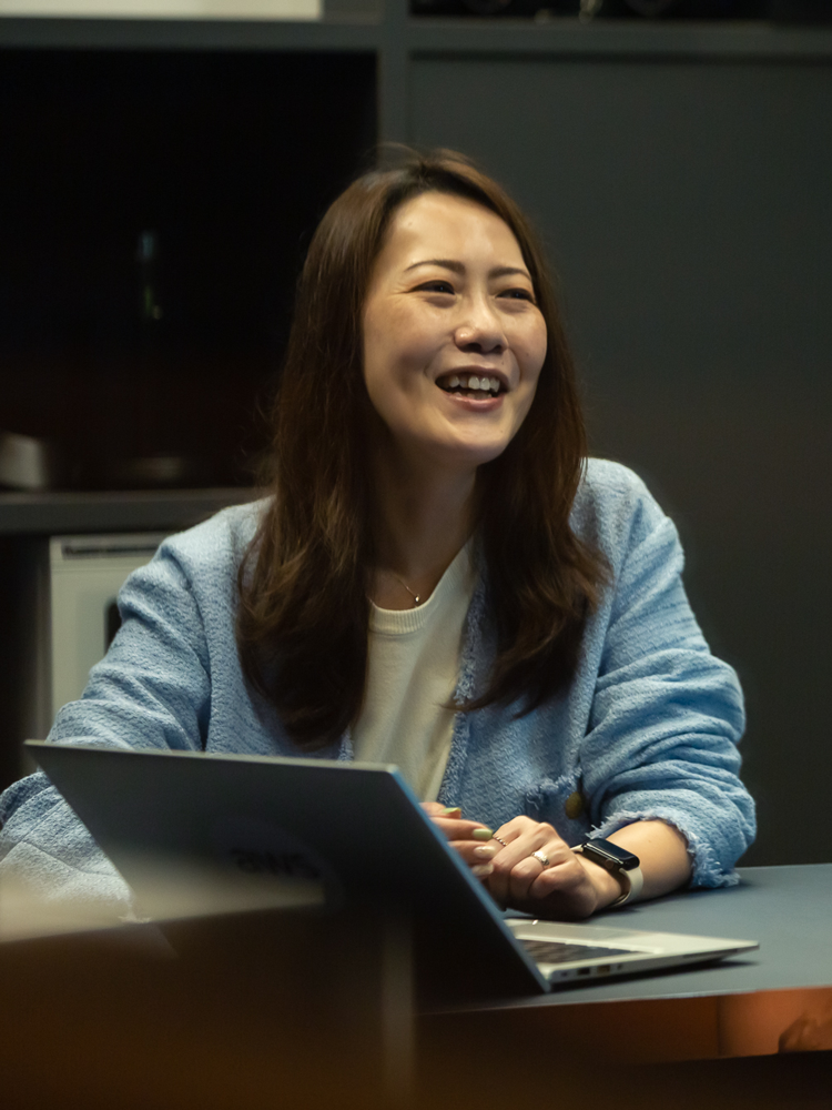 A woman smiling while sitting at a desk with a laptop.
