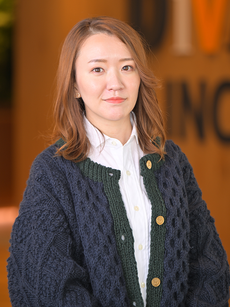 A professional portrait of a woman wearing a blue cardigan, posed in an office environment.