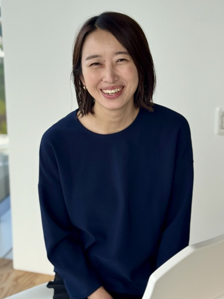 A woman smiling in an indoor setting, wearing a casual navy top. Portrait orientation.